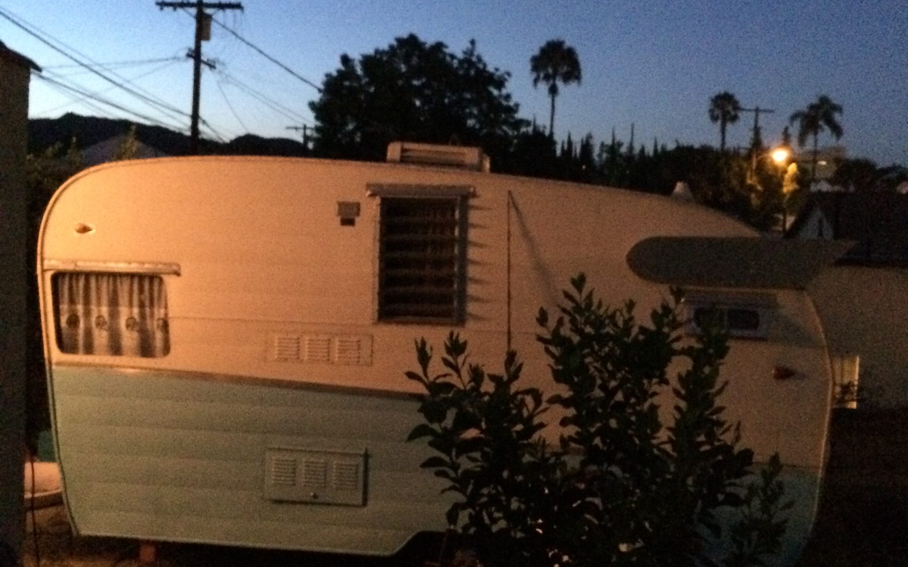 A two-tone mint and white vintage Shasta travel trailer at dusk, palm trees against a deep blue sky